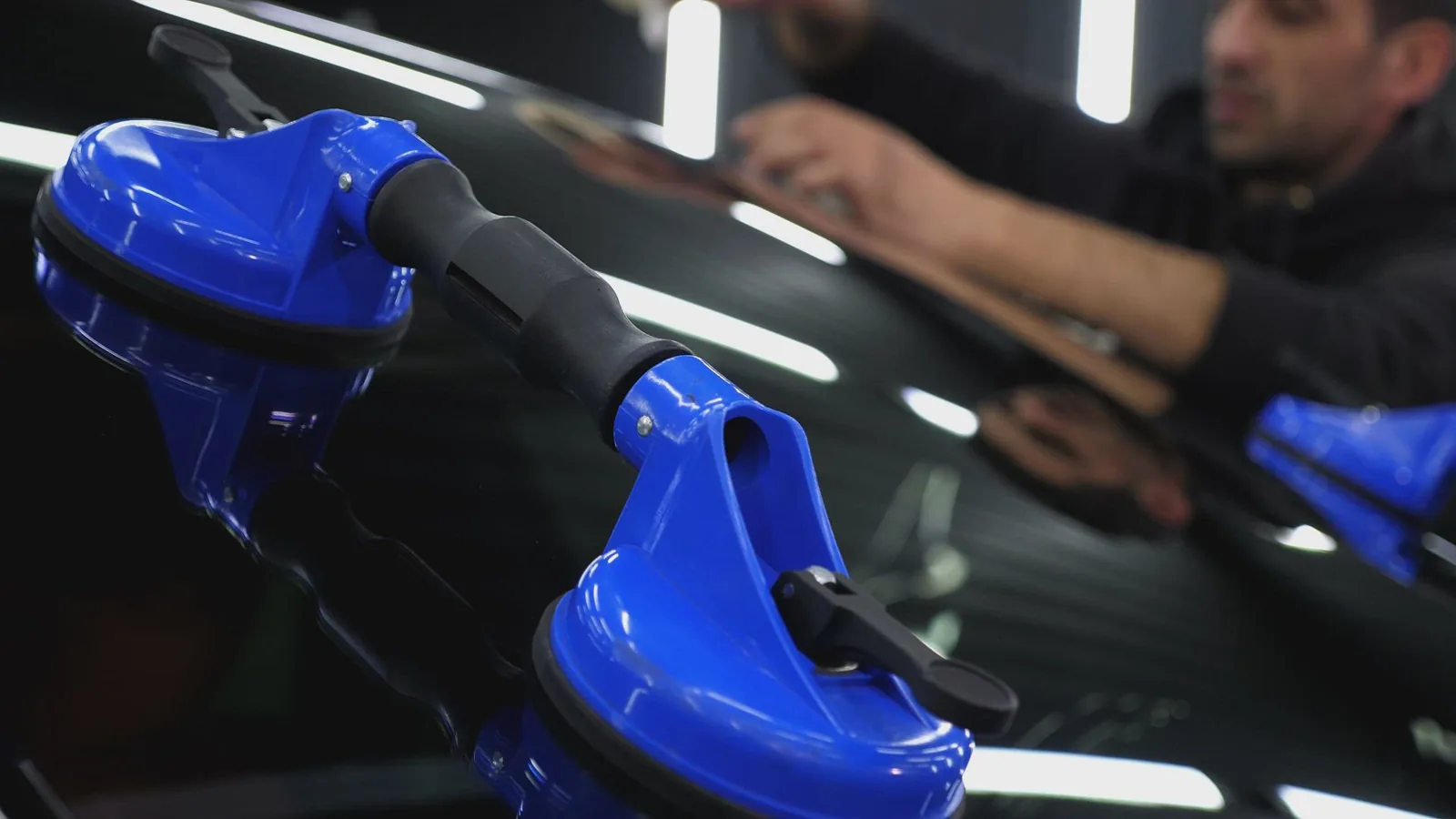 Auto glass technician handling a windshield with suction tools